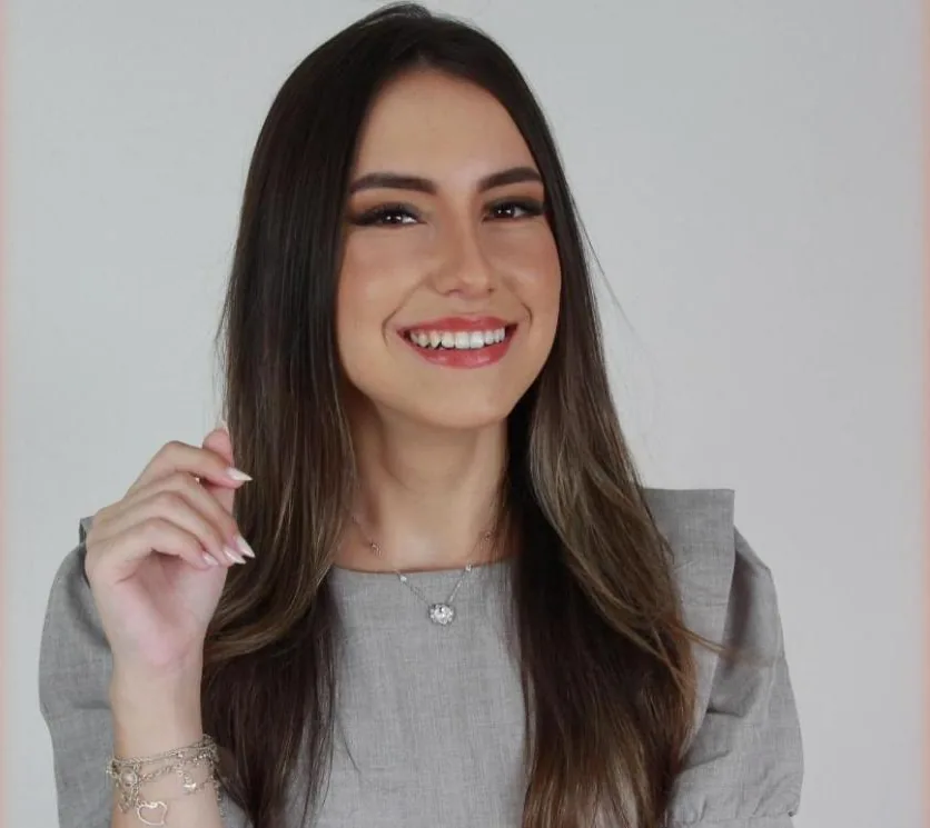 Giulia Doratiotto sorrindo, de blusa cinza, mão perto do rosto